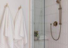 Shower features pink floor tiles, white vertical stacked shower tiles with a satin nickel shower kit, a built in shower bench and a glass partition.