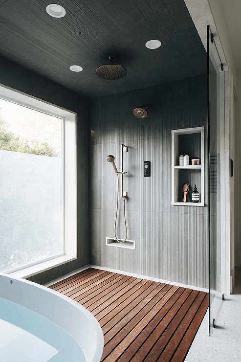 Large walk-in shower boasts a glass partition and a teak slatted floor, as black striped wall tiles frame stacked niches fixed beside a satin nickel shower kit under a black striped ceiling.