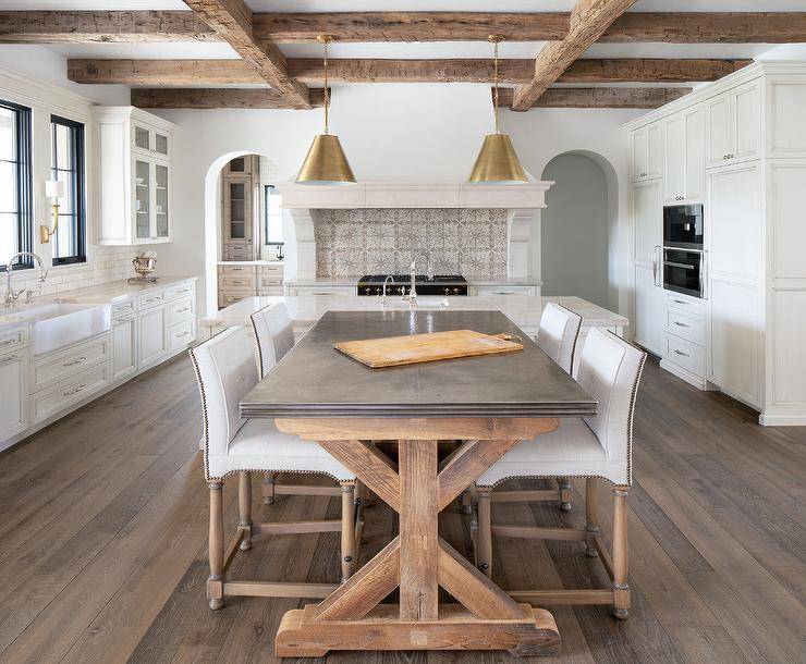 Rustic wood ceiling beams complement a dining space boasting a wood and zinc trestle dining table surrounded by white nailhead chairs.