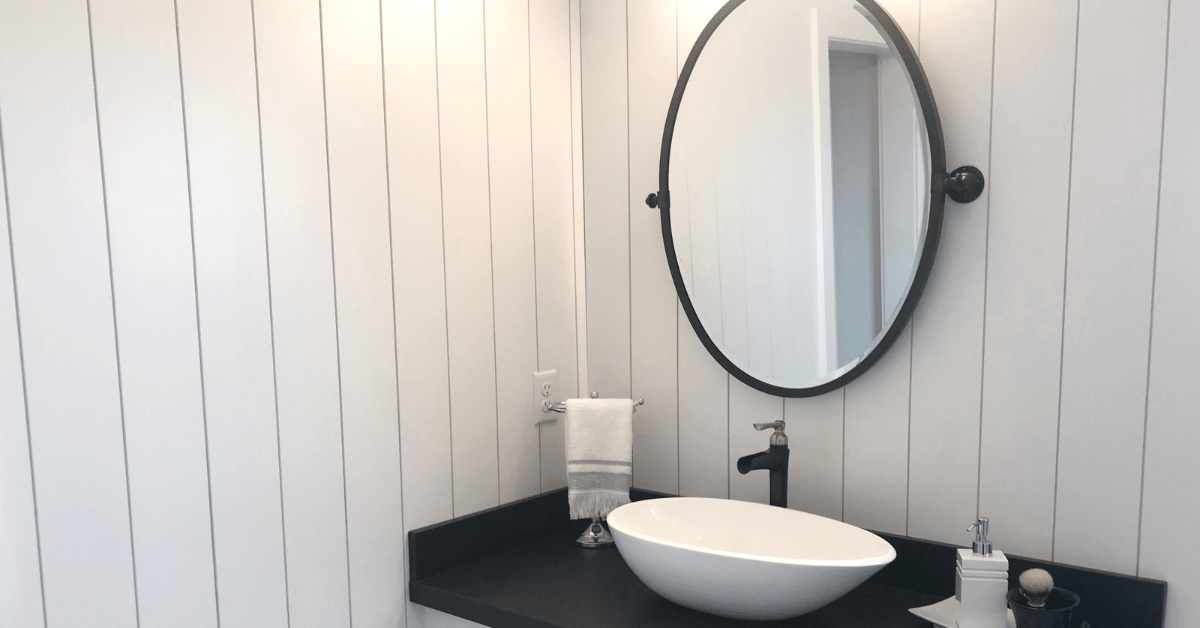 Shiplap walls in a bathroom with round mirror.