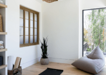 A stunning wicker chandelier is fixed over a black yoga mat placed on a wood floor, while a gray floor pillow is placed in front of a picture window.