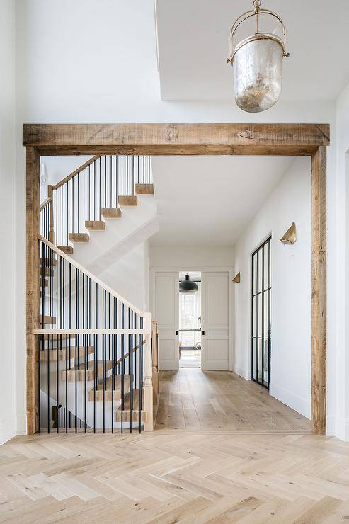 Cottage style foyer features light wood herringbone floors and a wrought iron staircase illuminated by a mercury glass lantern.