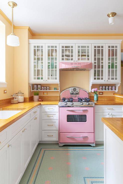 Northstar pink range with a pink retro hood finished with white glass front cabinets, blond wood countertops, and charming green and pink floor tiles in a lovely vintage kitchen.