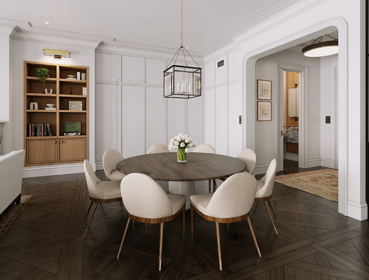 Dining space features linen and walnut dining chairs at a round walnut dining table on parquet wood floors, illuminated by a square lantern and brown built in shelves.