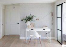 A white chair sits on a gray wash wide plank wood floor at a white desk, styled and placed in front of a gray wallpapered wall.