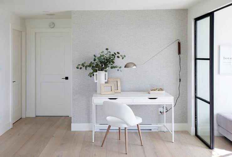 A white chair sits on a gray wash wide plank wood floor at a white desk, styled and placed in front of a gray wallpapered wall.