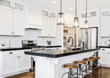 A bright white kitchen with black countertops and rustic stools.