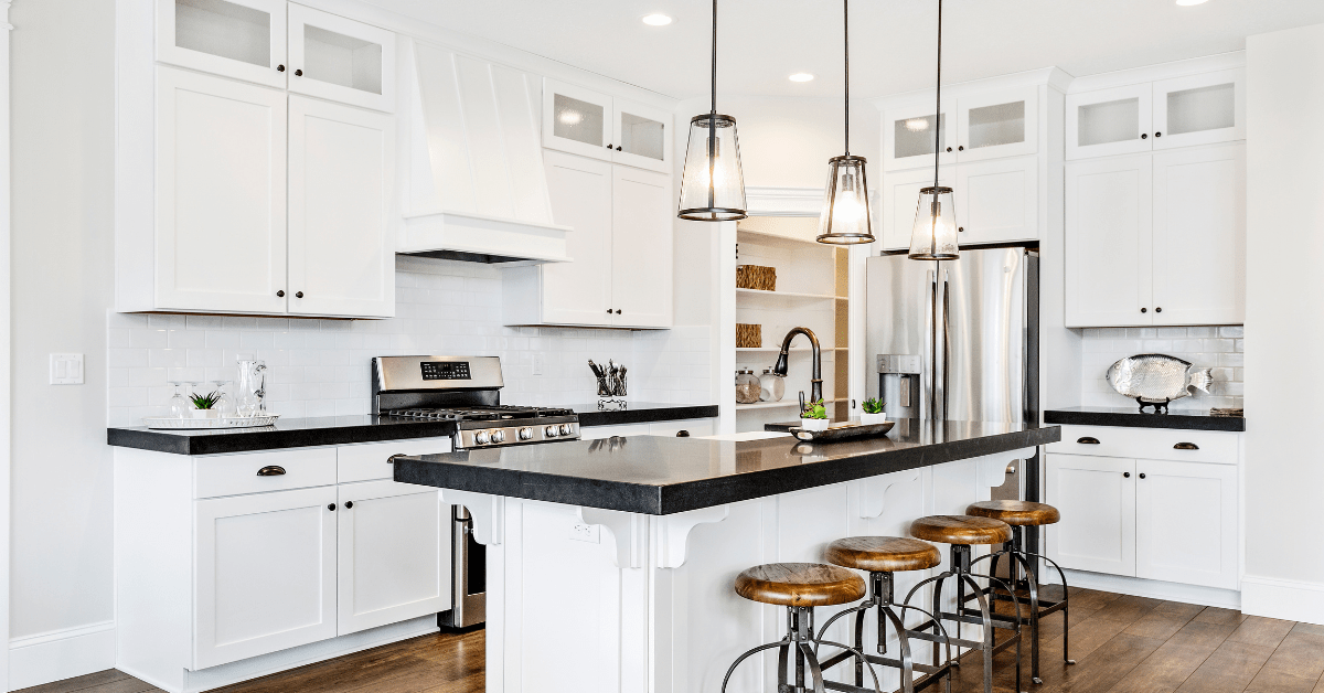 A bright white kitchen with black countertops and rustic stools.