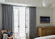 Gray curtains cover French doors located behind a vintage cane chair placed in a corner with a black and white round stool.
