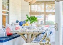 Beautiful enclosed patio boasts shiplap walls and wicker lanterns hung over a plank trestle dining table seating blue French bistro chairs facing a beadboard dining bench topped with blue cushions.