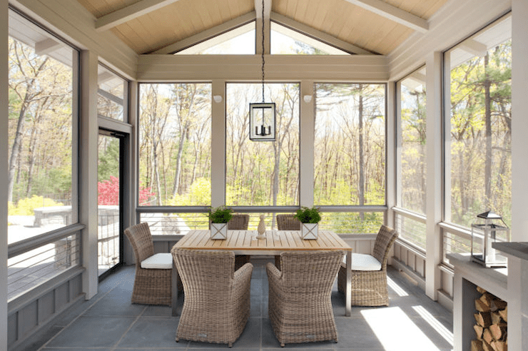 Enclosed patio with wood plank vaulted ceiling and modern lanterns hangs over teak dining table with polished chrome legs.Teak dining table surrounded by wicker dining chairs over slate tile floor.