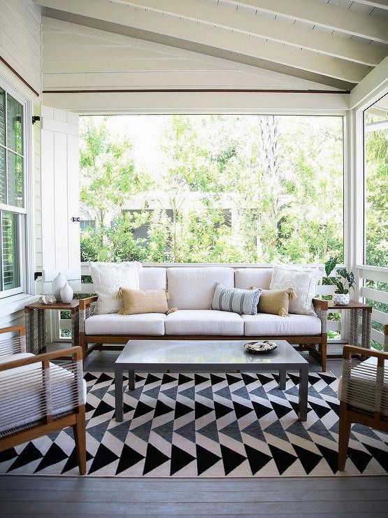 Enclosed patio features a brown wooden and gray rope sofa and a gray lacquer coffee table atop a black, gray and cream geometric rug.