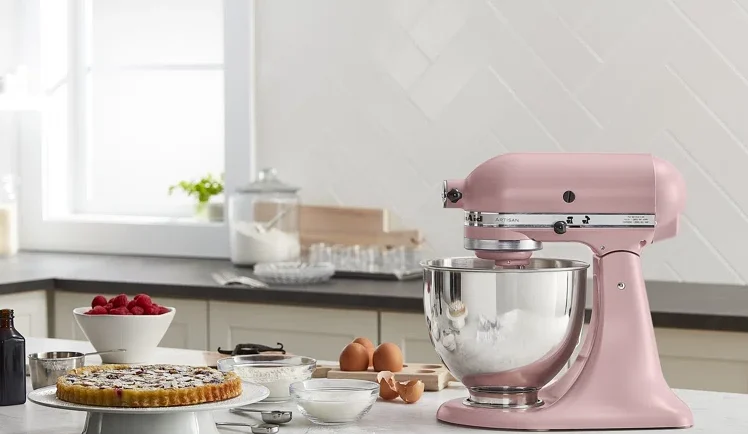 kitchen aid stand mixer pink on marble countertop with baking supplies and pies around it