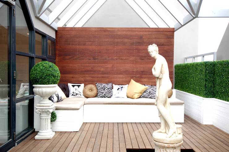 Contemporary patio features vaulted glass ceiling over L shaped built-in seating accented with black and white zebra pillows, gold pillows and fashion pillows as well as Greek statue placed in center of space.