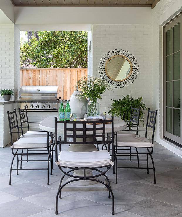 Wrought iron dining chairs sit around an oval marble dining table placed inside a small enclosed patio.
