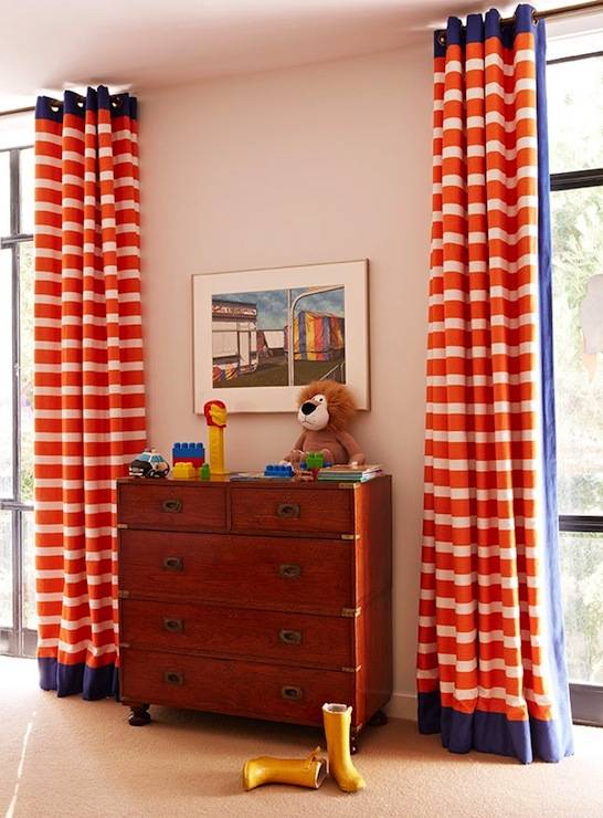 Blue and orange boy's bedroom with vintage campaign style chest flanked by windows covered in floor to ceiling orange and white striped grommet drapes.