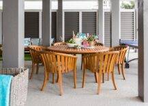 Contemporary covered patio furnished with a round teak dining table and curved teak chairs displaying a summer themed tablescape.