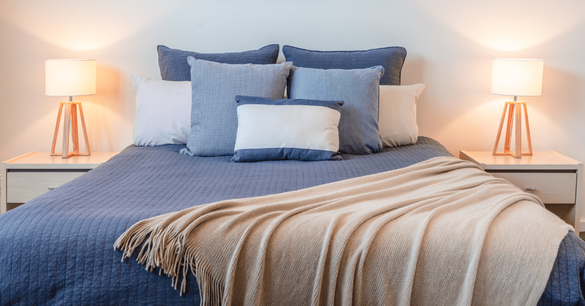 A blue bed with soft colored throw blanket.