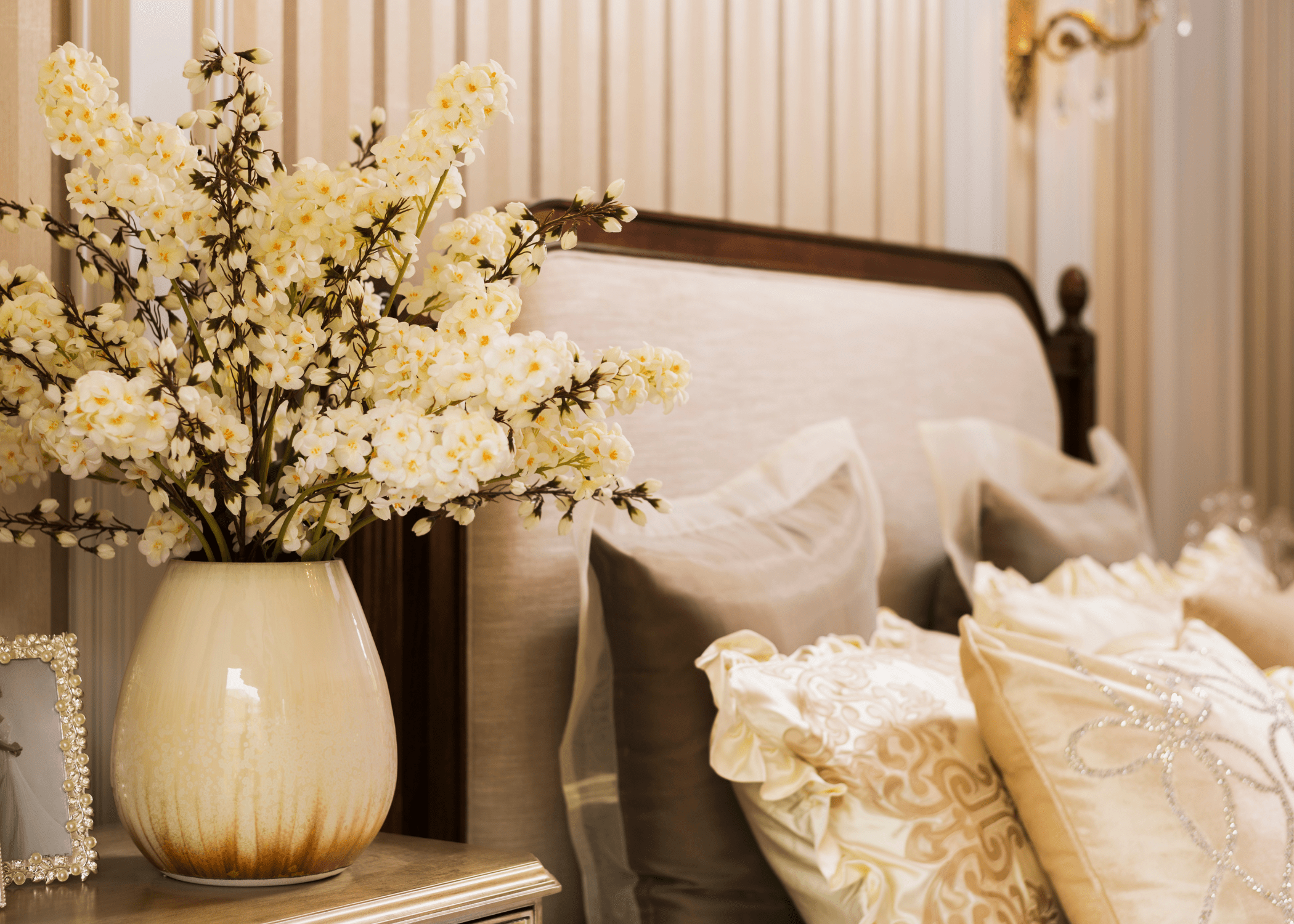 close up of the upper portion of a bed with vase of faux flower stems on nightstand