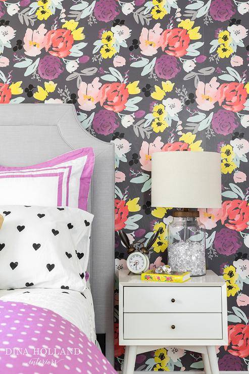 Dove gray and purple girl's bedroom stands out with an accent wall covered in Caitlin Wilson Blooms Grande in Grey Wallpaper located behind a dove gray velvet headboard complementing a bed placed dressed in a purple polka dot duvet covering a black and white hearts sheet set finished with purple border shams while beside the bed, a West Elm Mid-Century Nightstands is topped with filled glass jar lamp.
