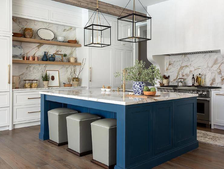 Three gray storage ottomans double as counter stools tucked under a bold blue wooden kitchen island illuminated by square black lanterns.