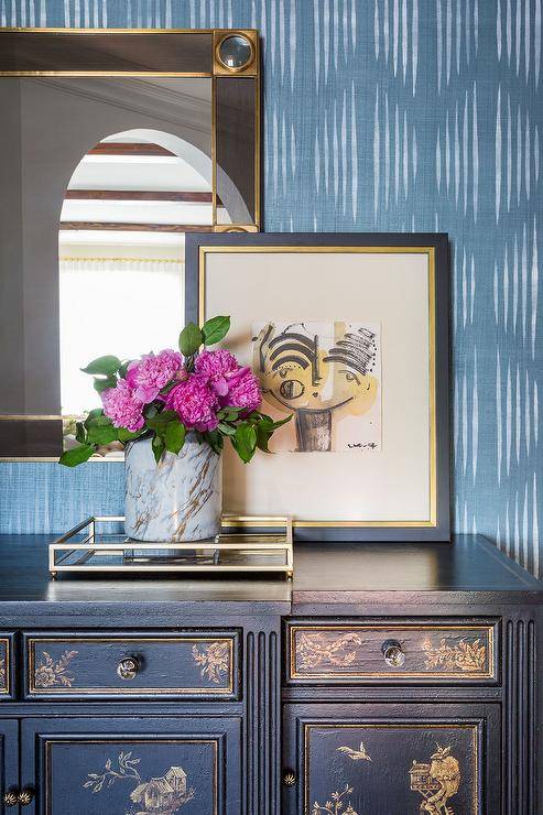 Art deco mirror over a black and gold vintage dresser displaying a glass gold tray with a marble vase and pink florals for a fresh, sophisticated appeal. Gold leaf trim accents the French antique style dresser with a dainty and intricate design.