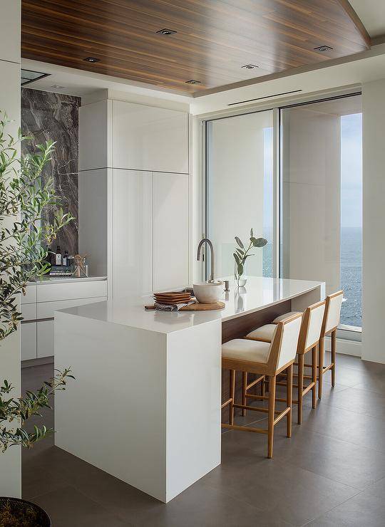Kitchen features ivory fabric and brown wood stools at a modern center island with nickel gooseneck faucet.