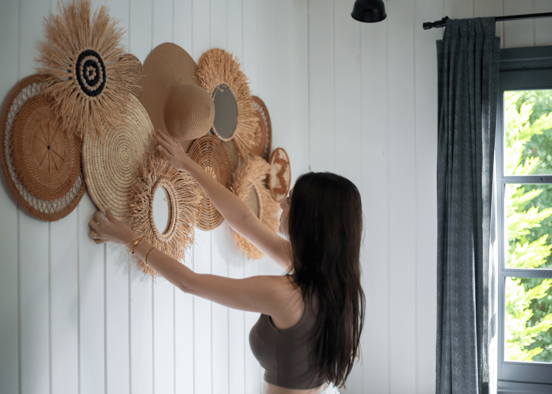 woman hanging up rattan wall art on white shiplap wall