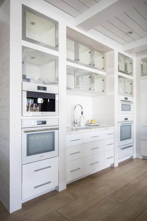 Modern kitchen pantry features white appliances and white cabinets with stainless steel framed cabinet doors
