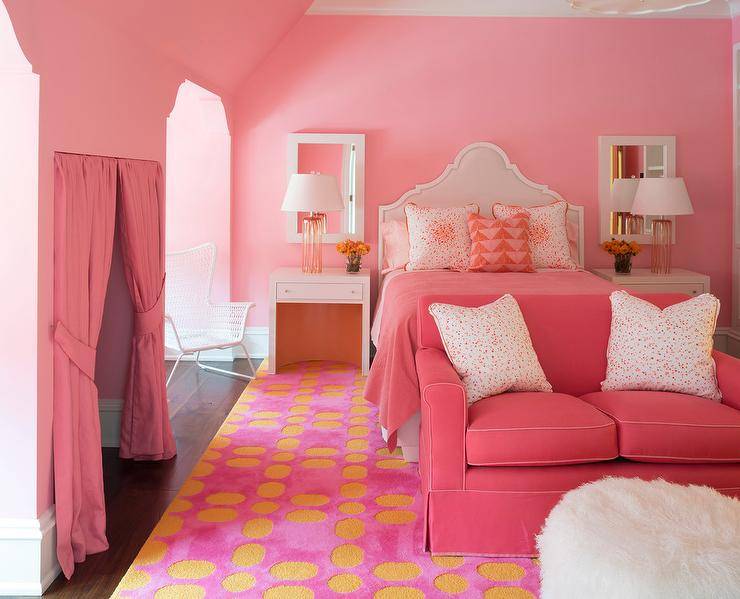 Adorable contemporary pink girl's bedroom with yellow accents features a white arched headboard positioned against a pink wall behind a bed dressed in pink pedding topped with pink splatter pillows flanked by white open nightstands placed under white Parson's mirrors and lit by glass table lamps. Two window nooks flank a pink curtain covered nook as a pink loveseat sits on a pink and yellow rug in front of the bed facing a white faux fur ottoman.