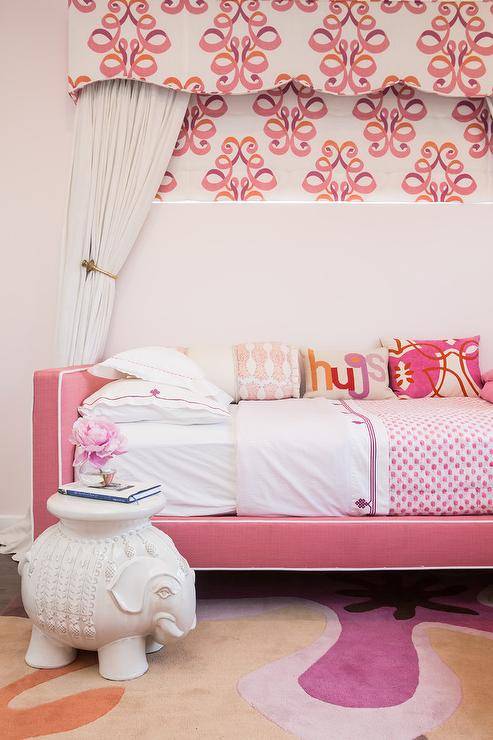 If your little girl loves pink, she'll adore this girl's bedroom fitted with a pink daybed accented with white piping and placed beneath a pink and orange valance fiished with white curtains. In front of the bed, a Serena & Lily Ellie Side Table sits atop a pink and beige rug.