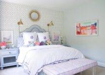 Soft pastel colors and a classic style will keep this girls room timeless. Trellis wallpaper walls with gold accented mirror and Boston Functional Library Wall Lights create a chic vibe across the wall and allow a curved purple headboard and monogrammed bedding to be the center of attention. Blue nightstands are decorated with floral arrangements and accessories while framed wall art is featured over them. A purple zebra bench with lucite legs is seated at the end of this luxe bed adding a dimensional and fun pattern!
