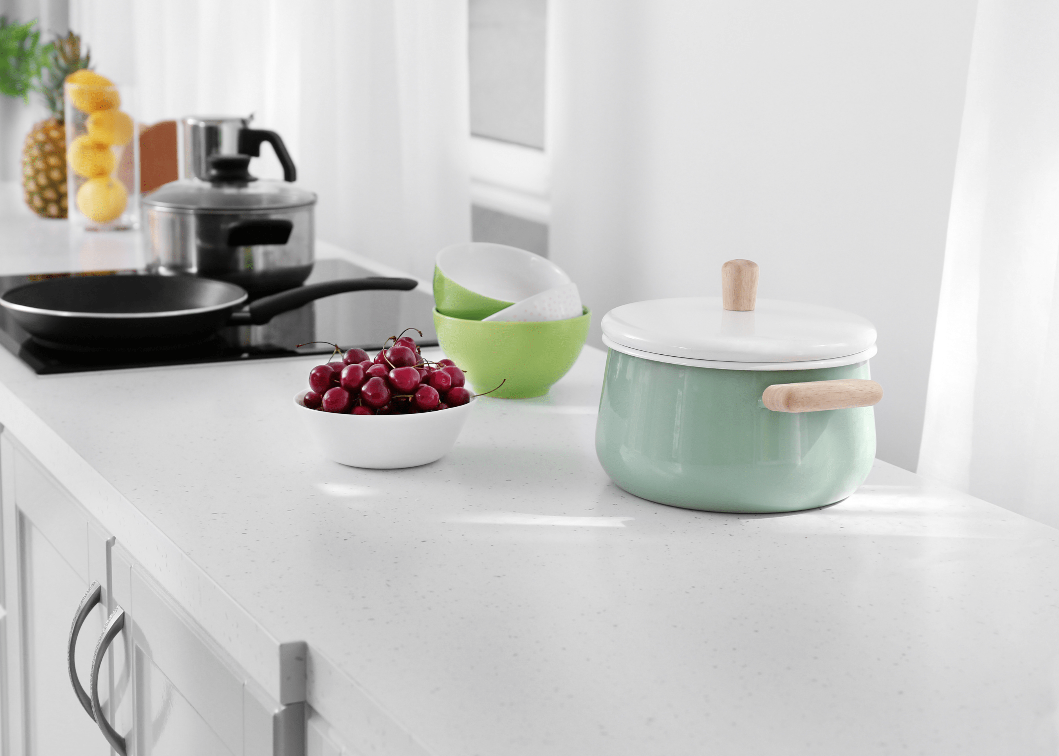 close up of white laminate countertop with sea foam green pot white bowl of cherries and black cooktop