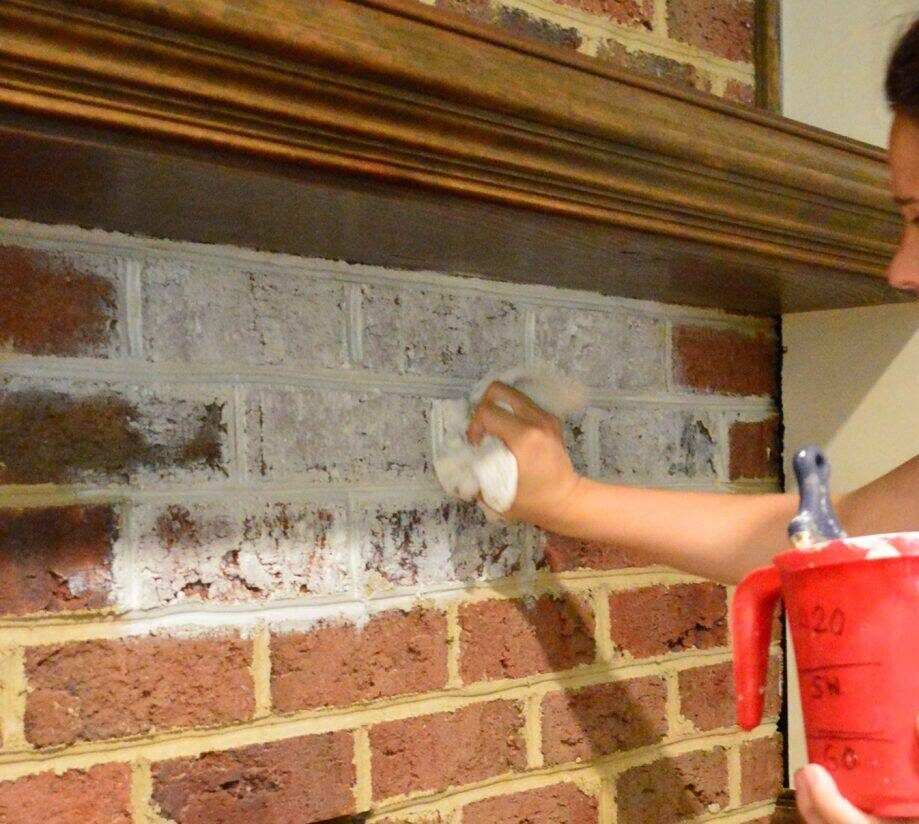 A closeup of someone applying paint to whitewash a fireplace.