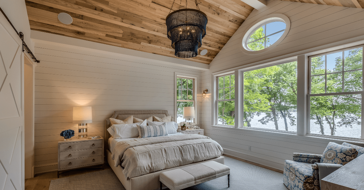 A modern bedroom with sloped wood ceiling and black chandelier.