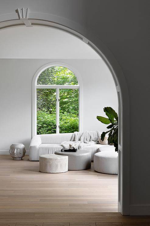 Living room features a low white couch with faces accent table, ottomans as coffee tables and an arch window.