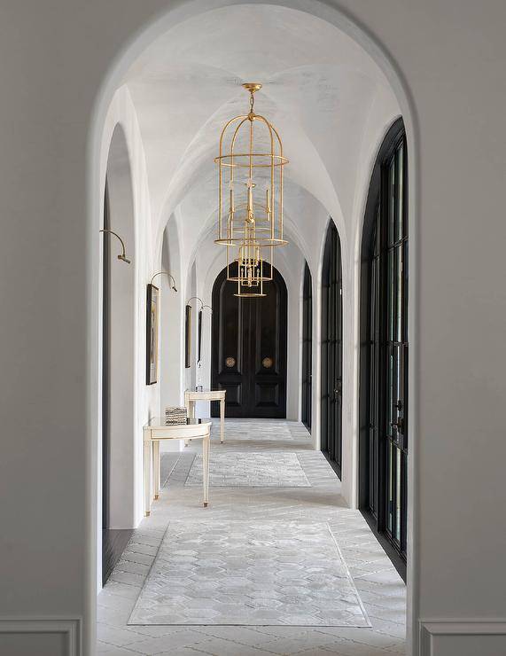 Gold lanterns hang from a stunning cloister ceiling in a hallway lined with black arch French doors.