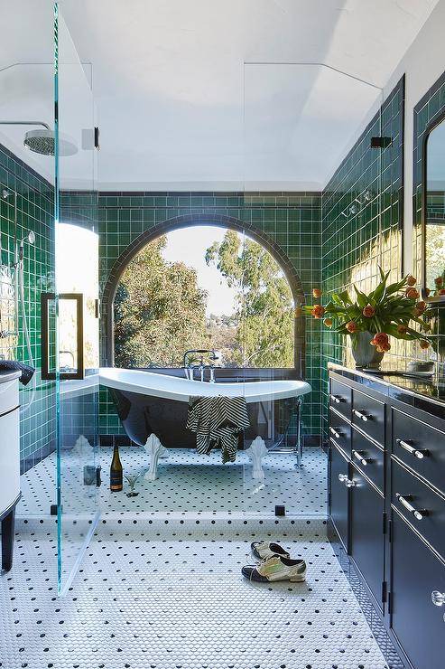 Bathroom features a walk in shower with a black and white clawfoot bathtub on black and white penny shower floor tiles, green grid shower wall tiles with an arch window, a clear shower partition and a black vanity.