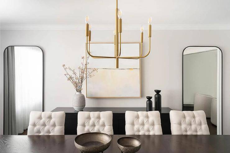 Dining room features ivory tufted dining chairs at a dark brown oak table illuminated by a brass chandelier.