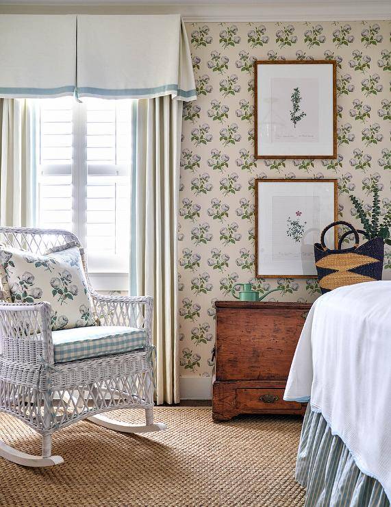 White rattan rocking chair in a shabby chic cottagecore bedroom near a window fitted with a linen and blue window treatments.