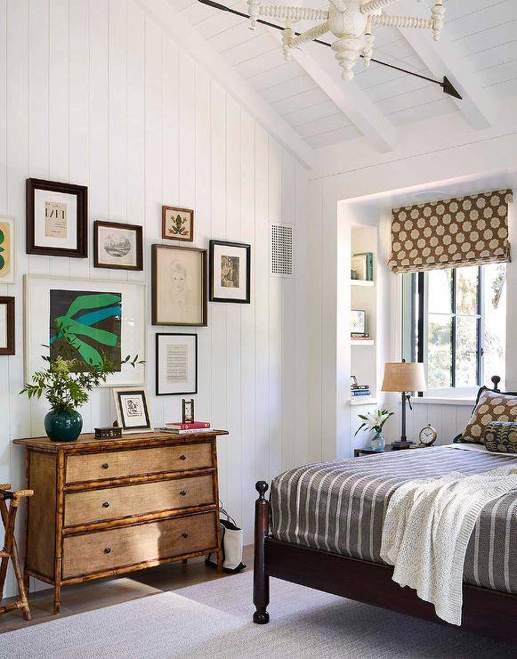 A vertical shiplap wall is accented with an art gallery hung over a bamboo dresser styled with a jade green vase in a cottagecore bedroom.