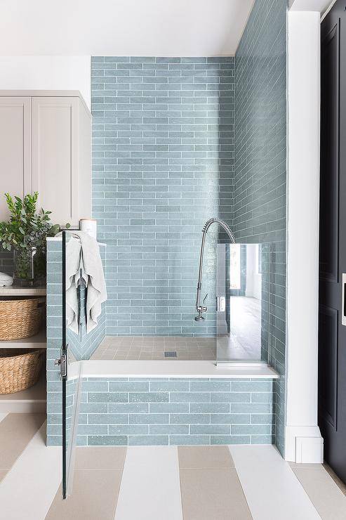 Pet friendly laundry room features white and taupe striped floor tiles finishing at a blue glazed offset tiled dog shower boasting a glass door and taupe grid floor tiles.