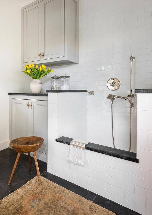 A tan vintage rug sits on slate floor tiles in front of a white subway tiled dog shower fitted with a polished nickel shower kit.