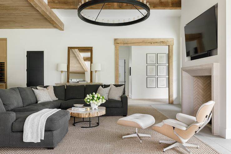 A black wagon wheel chandelier illuminates a wonderfully styled living boasting a round industrial coffee table placed on a bound sisal rug in front of a charcoal gray sectional complemented with light gray pillows.