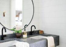 Cottage bathroom with an industrial touch features a white washstand with a concrete countertop and oil rubbed bronze faucets. A shiplap wall sets a farm style surface for round black mirrors and a black farm style sconce.