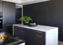 A honed marble waterfall edge countertop accents a black veneer center island finished with brass pulls.