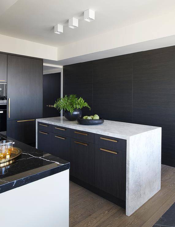A honed marble waterfall edge countertop accents a black veneer center island finished with brass pulls.