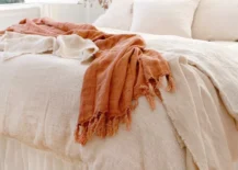 terracotta colored throw on white blanketed bed