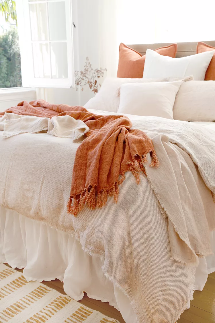 terracotta colored throw on white blanketed bed
