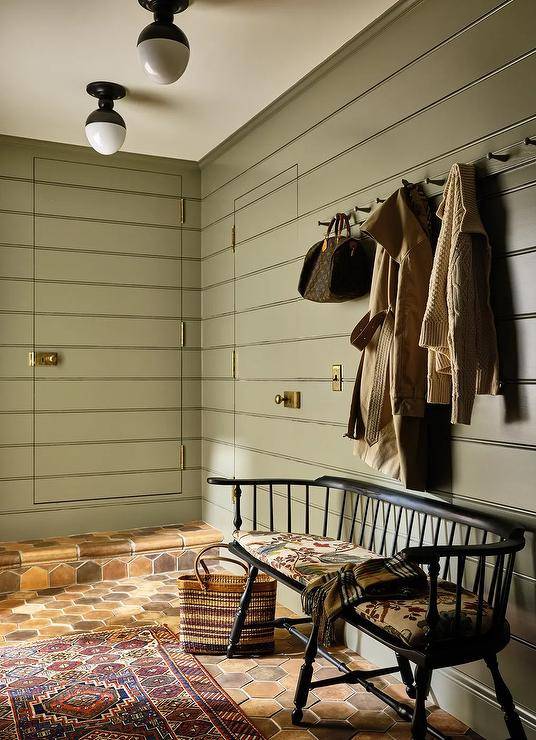Green shiplap mudroom features a jib door and a black vintage bench on terracotta hexagon pavers.